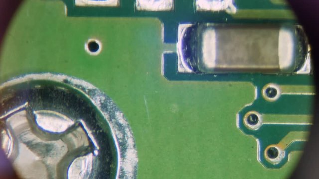 View through the eyepiece of the microscope of the mounting electrical board. The master moving the board inspects it for damage