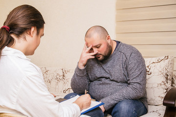 Depressive sad fat man talking with psychologist about his problems. Psychologist writes notes