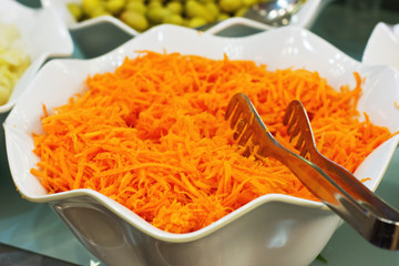 Grated fresh carrots in a white bowl with a silver spatula