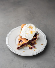 A piece of cherry pie with vanilla ice cream on a white vintage plate on a gray light concrete background. Copy Space. View blank space for text.