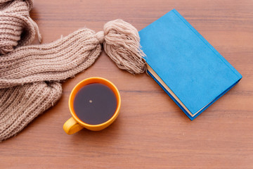 Cup of coffee, knitted scarf and book on wooden background