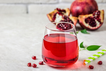 A glass with fresh pomegranate juice and pomegranate fruit on white marble background. Selective focus, copy space.