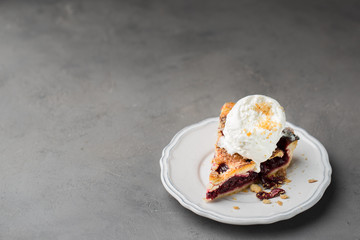 A piece of cherry pie with vanilla ice cream on a white vintage plate on a gray light concrete background. Copy Space. View blank space for text.