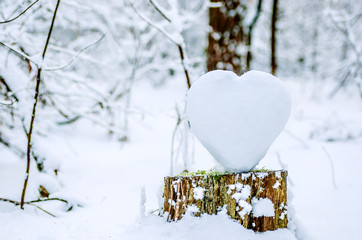 A large beautiful heart of snow stands on a stump in the winter forest. 