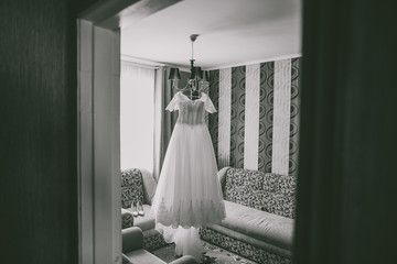 Bridal wedding drass hanging in home interior. Morning of bride concept. Horizontal black and white photography.