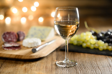 glass of white wine with french cheese and delicatessen in restaurant wooden table with romantic dim light and cosy atmosphere