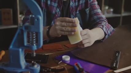 Handmade leather manufacturing. Craftsman making leather purse. Craftsman hands doing leather impregnation in home workshop. Craft man manufacturer processing finished product