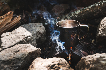 Metal cup with tea coffee water warming on fireplace outdoors.