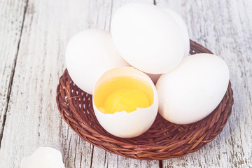 Broke One whole egg amongst white eggs in basket on a white wooden background