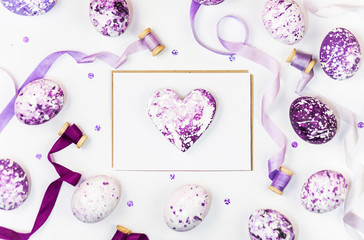 Easter composition with heart, painted eggs, sequins and silk ribbons on a white background. Space for a greeting text. Easter, spring concept. Flat lay, top view.
