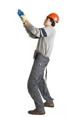 A young man in working grey clothes and orange hard helmet putting on a glove on white isolated background.