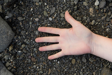 Female open palm with french manicure with the fingers spread lies on black pebbles