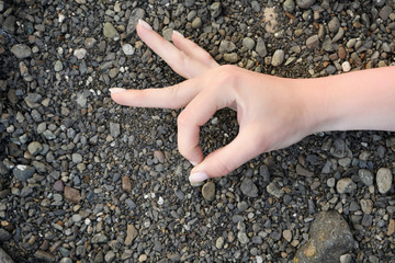 Female hand folded as a sign of OK is on the sea pebbles black grey