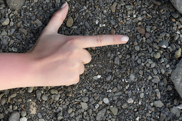 Female hand folded in the sign of the gun is knuckles to the top of marine gravel black gray