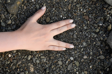 Female hand folded in a sign of the Vulcan Salute is on the sea pebbles black grey