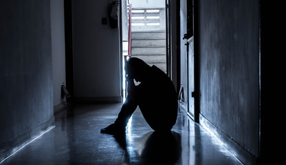 Silhouette of a sad young man sitting in the dark leaning against the wall with his back, The sun...