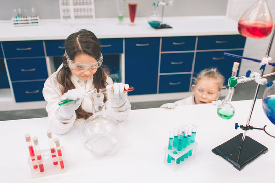 Two little kids in lab coat learning chemistry in school laboratory. Young scientists in protective glasses making experiment in lab or chemical cabinet. Studying ingredients for experiments .