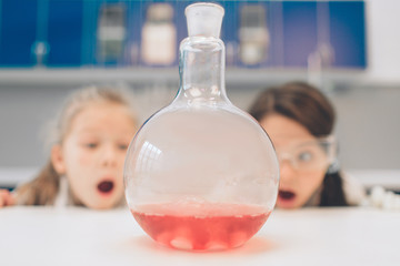 Two little kids in lab coat learning chemistry in school laboratory. Young scientists in protective glasses making experiment in lab or chemical cabinet. Studying ingredients for experiments