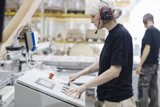 Side view of female worker wearing ear protectors operating machine at industry