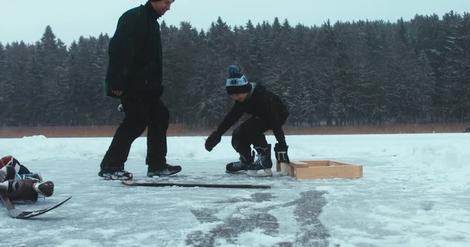 Father helps his son to lace hockey skates before playing pond hockey on a frozen lake. 4K UHD