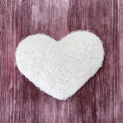 Hand knitted white heart on a wood texture background. The figure of the heart is connected with white thread. Flat lay.