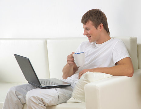 Young man sitting on sofa with laptop and a cup of coffee