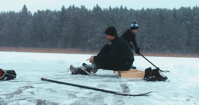 Father lacing his hockey skates before playing pond hockey with his son on a frozen lake. 4K UHD