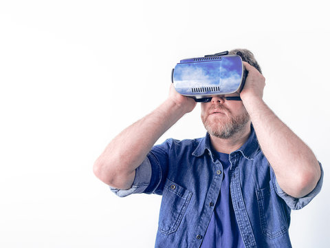 A man in a blue denim shirt wore a game helmet on his head and watches the virtual clouds. Image on the theme of augmented or virtual reality, visual technologies and games