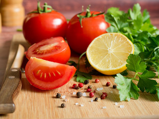 Fresh vegetables Tomatoes Lemon Parsley Pepper coarse Salt and a Knife on a cutting Board