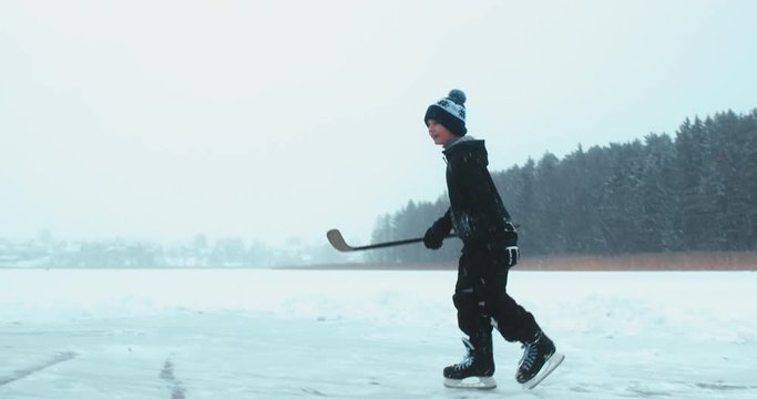 Kid celebrates after scoring a goal in pond hockey game on a frozen lake ice surface. 4K UHD