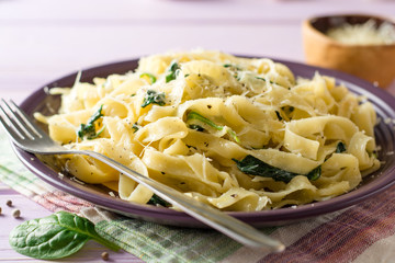 Tagliatelle pasta with spinach, garlic and Parmesan cheese on purple wooden background.