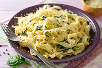 Tagliatelle pasta with spinach, garlic and Parmesan cheese on purple wooden background.
