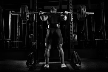 Professional athlete is standing with a barbell on his shoulders and is about to sit down with her.