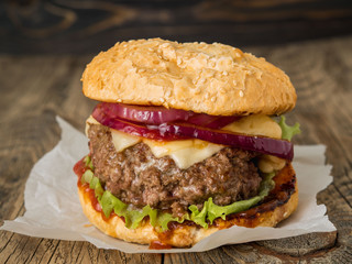 delicious homemade burger with beef cutlet, cheese, onion, tomato and lettuce on toasted rolls. American fast food, unhealthy eating.  Side view, selective focus