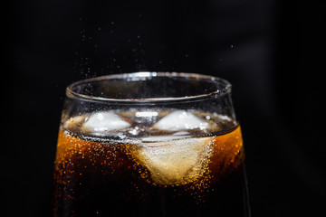 A glass of cola beverage with a salt. On a black background.