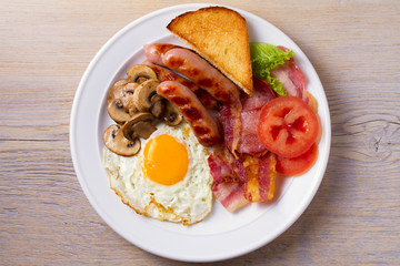 Traditional English or Irish breakfast: sausages, bacon, egg, mushrooms, tomatoes and toasts. Nutritious morning meal. View from above, top, horizontal