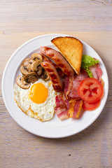 Traditional English or Irish breakfast: sausages, bacon, egg, mushrooms, tomatoes and toasts. Nutritious morning meal. View from above, top, vertical