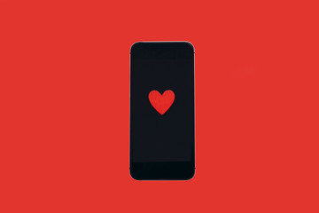 Top view. Heart on the phone screen which lies on a red background.