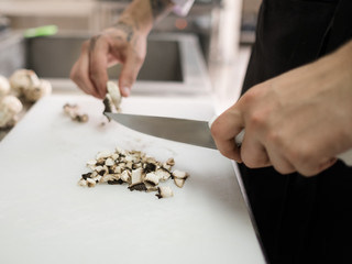 Chef cutting mushrooms in the restaurant kitchen. Food ingredients preparing before cooking tasty meal