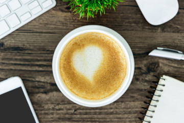 A latte coffee with art heart milk on the brown wood desk table from top view and copy space. Flat lay with desk, business and valentine concept.