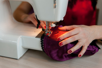 Female hands on sewing machine. Process of silk lingerie making. Close up of seamstress work.