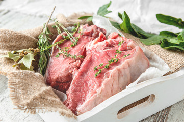 Cuts of beef for grilling on a wooden cutting Board with spinach, rosemary and Provencal herbs for the marinade in a rustic style.
