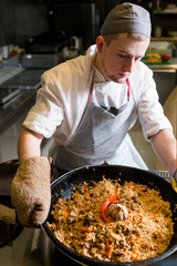 Chef cooking plov in the kitchen. Traditional famous Uzbek rice meal.