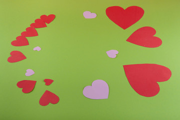 Holiday frame made of red, pink paper hearts on green background