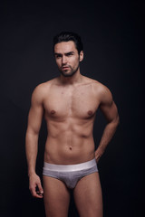 Fototapeta na wymiar one young handsome man, black background, shirtless wearing briefs only, posing, looking away.