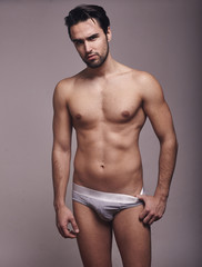 Fototapeta premium one young handsome man, looking at camera, shirtless, fashion model, gray background wearing briefs.