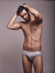 one young handsome man, looking at camera, shirtless, fashion model, gray background wearing briefs.