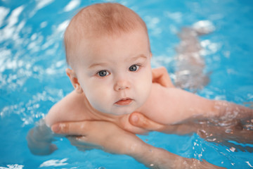 Fototapeta na wymiar Portrait of white Caucasian baby in swimming pool. Child training to swim float in water. Healthy active lifestyle