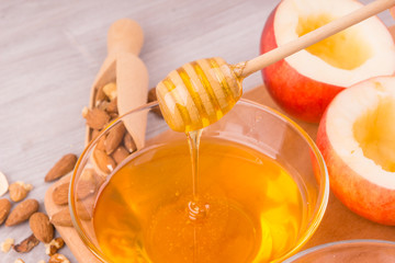 cup of honey, apples, wooden spoon and walnuts and almonds on light wooden background