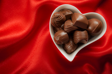 Romantic sweet gifts for Valentine's Day concept with a heart shaped box filled with chocolate pralines on red silk or satin with copy space
